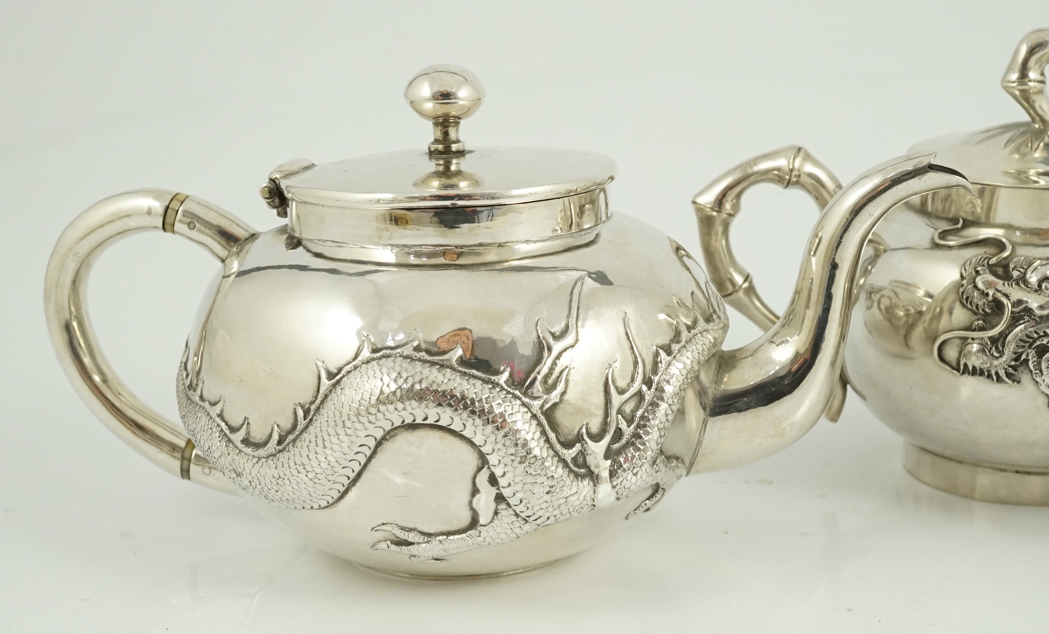 A Chinese three piece silver bachelor's tea set, by TC, decorated with dragon and one other similar Chinese silver two handled sugar bowl and cover, maker Sing Fat? and an odd cover